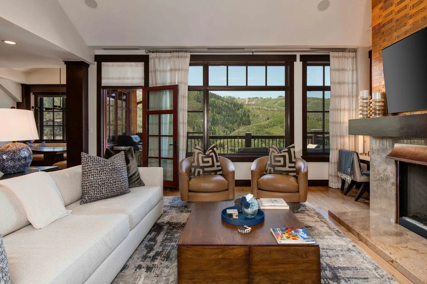 A living room with seating around a coffee table and large windows overlooking greenery.