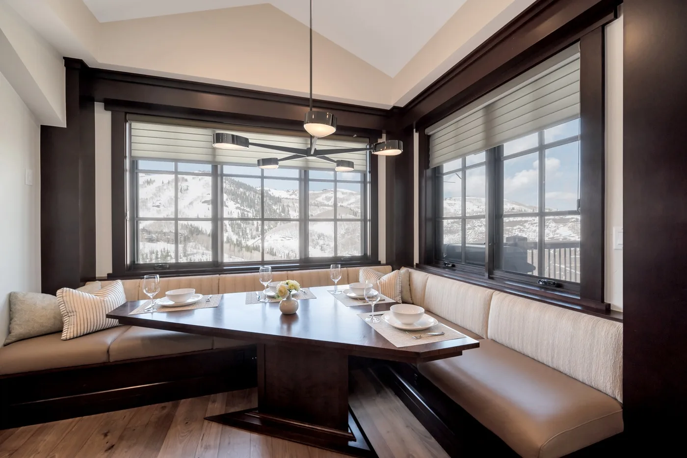 A dining nook with a dark table and cushioned seating beside large windows.