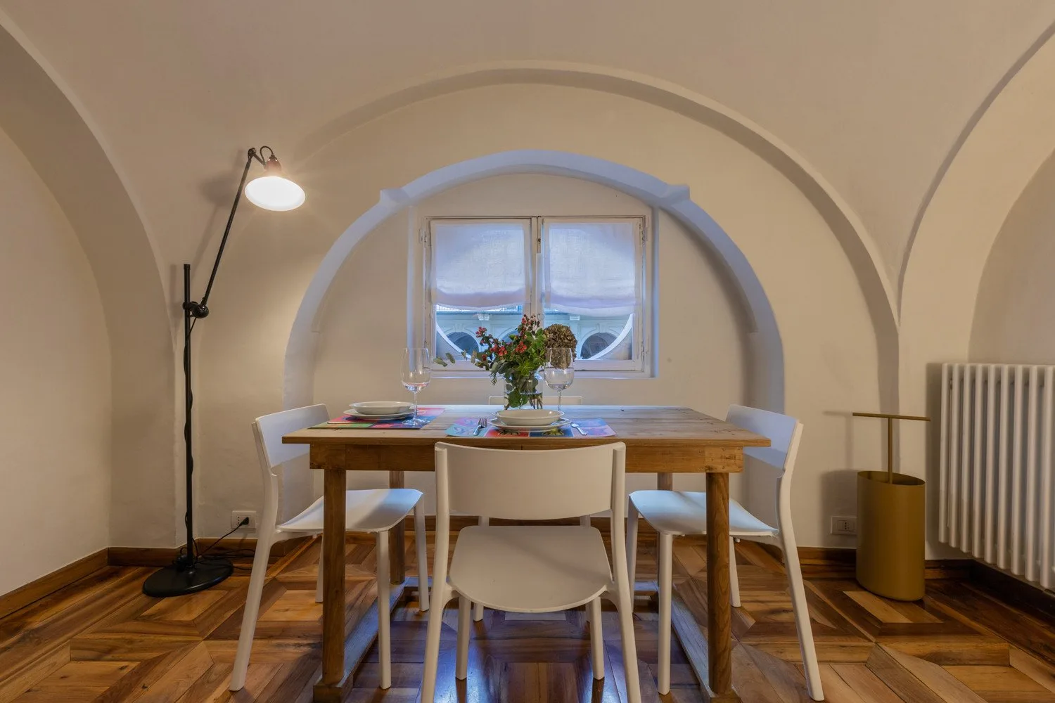Comedor con una mesa de madera y sillas bajo una ventana arqueada.