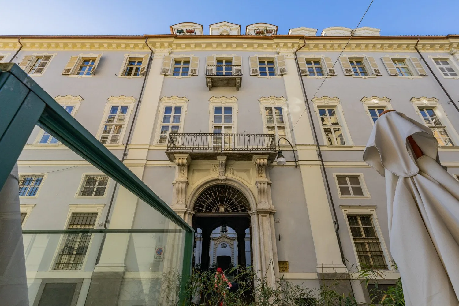 Un edificio claro de varias plantas con molduras decorativas en las ventanas y una entrada arqueada.