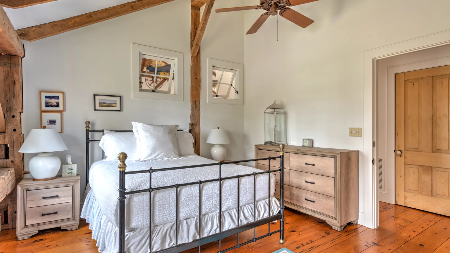 Un dormitorio con una cama de metal, una cómoda de madera y vigas expuestas.