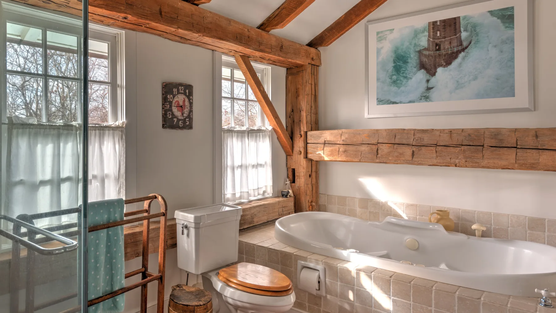 Un baño con bañera, inodoro y ventanas bajo vigas de madera expuestas.