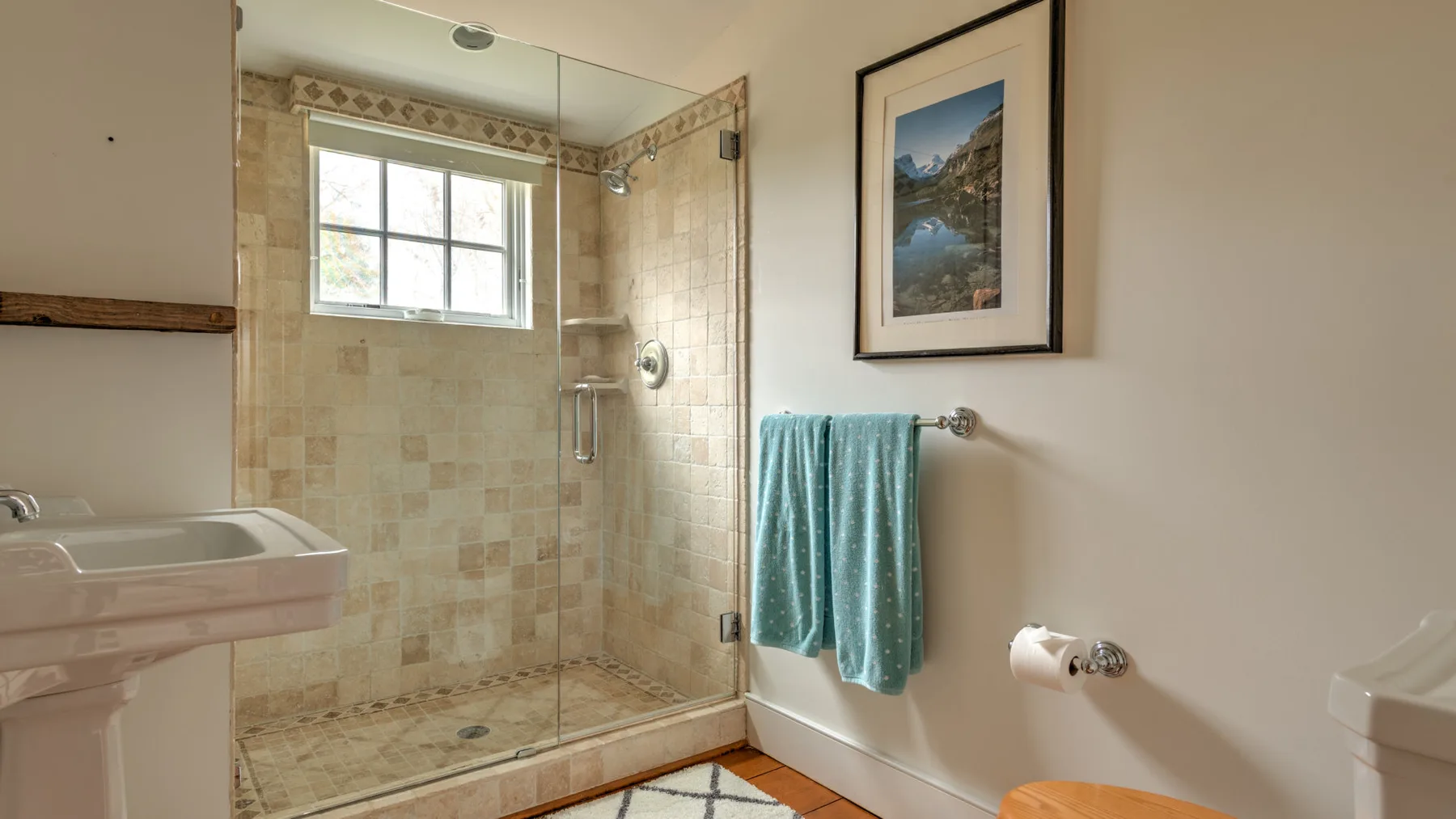 Un baño con ducha de vidrio, lavabo y toalla turquesa.