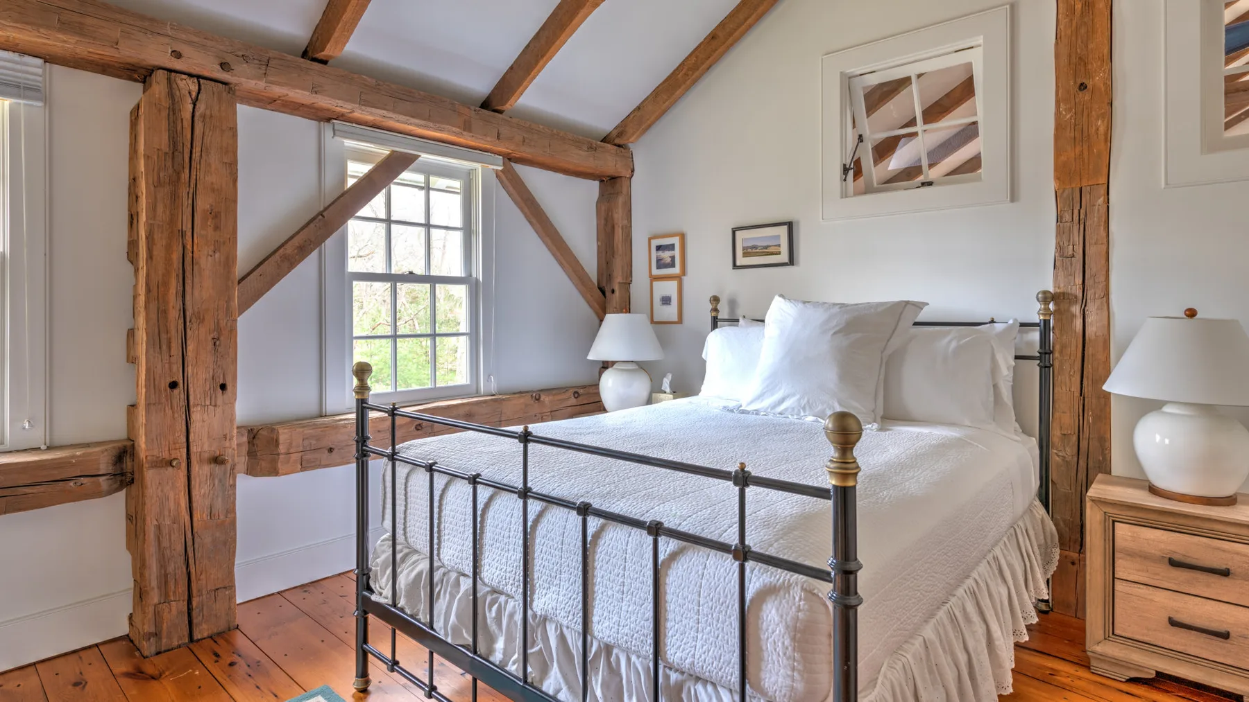 Un dormitorio luminoso con una cama blanca y vigas de madera a la vista.