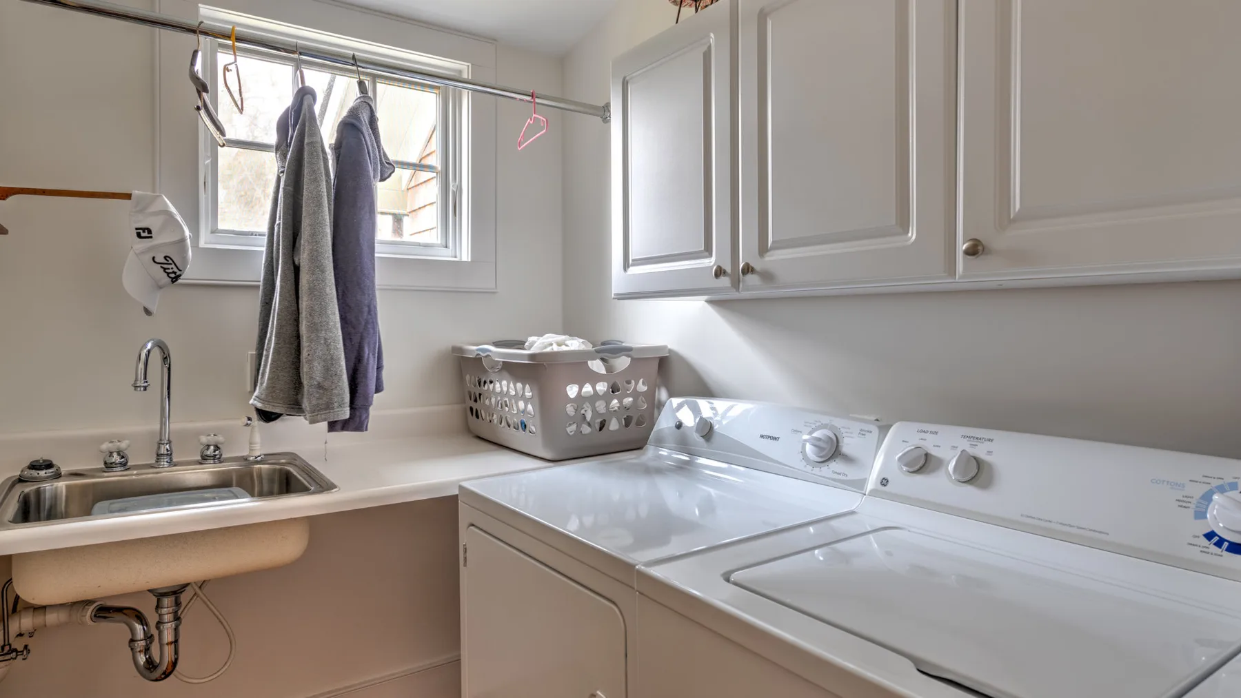 Un cuarto de lavandería con lavadora, secadora y fregadero bajo armarios blancos.