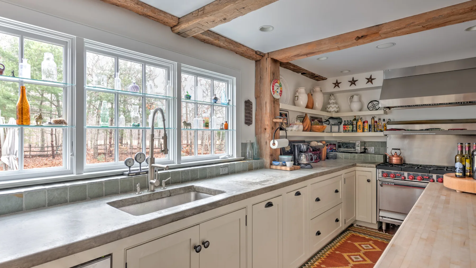 Una cocina luminosa con un fregadero bajo grandes ventanas y vigas de madera en el techo.