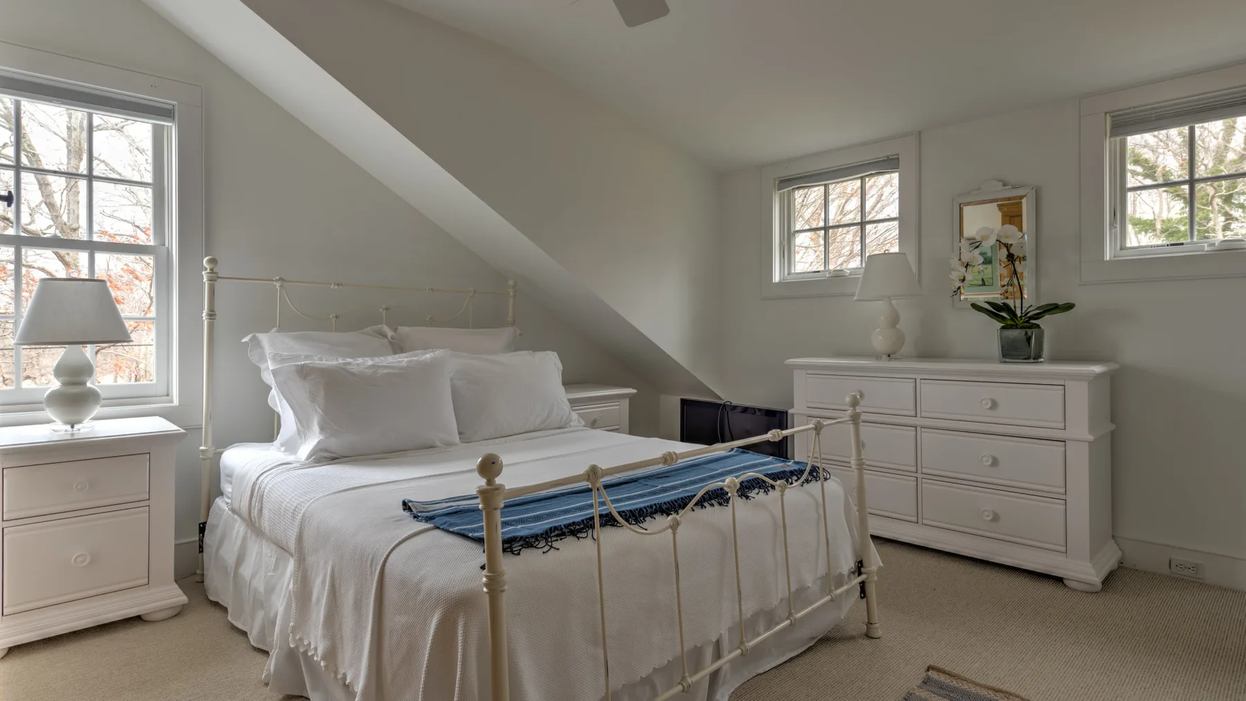 Un dormitorio luminoso con una cama bien hecha y varias ventanas.