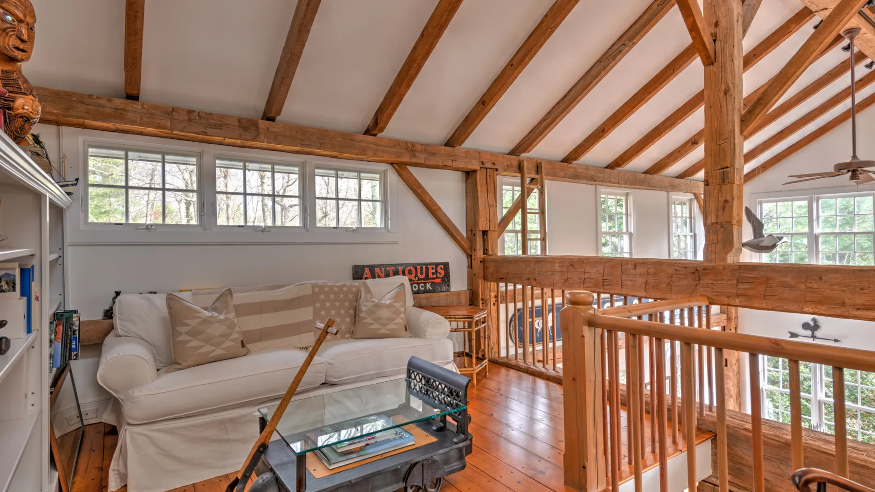 Una luminosa sala tipo loft tiene asientos blancos, vigas expuestas y barandillas de madera.