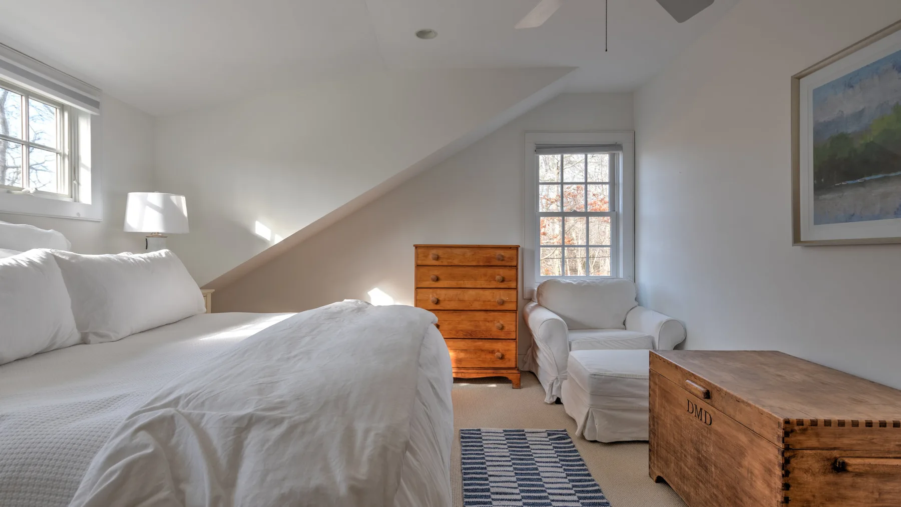 Un dormitorio luminoso con una cama, asientos y un baúl de madera.