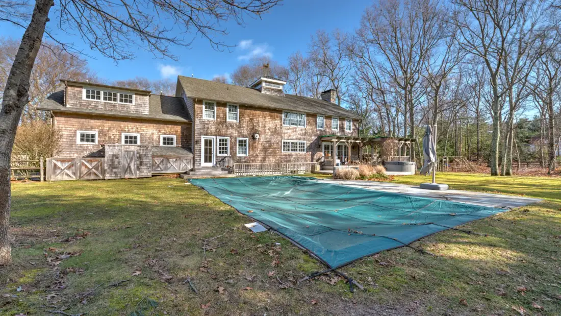 Una casa grande está junto a una piscina cubierta en un patio arbolado.