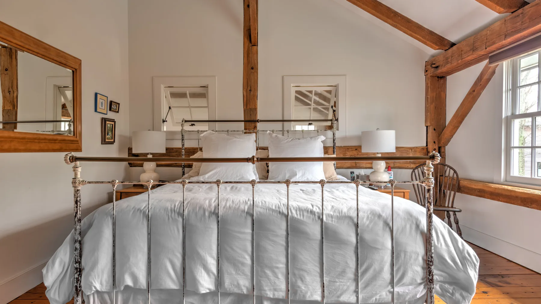 Un dormitorio con cama de metal, ropa de cama blanca y vigas de madera a la vista.