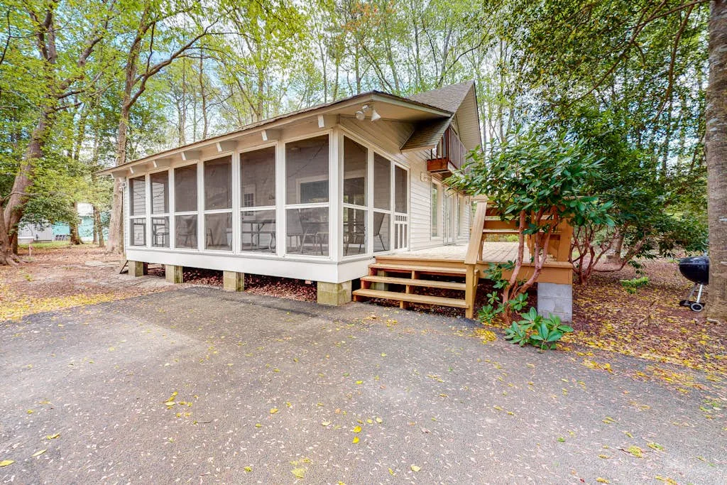 A screened cabin sits among trees beside a paved area.