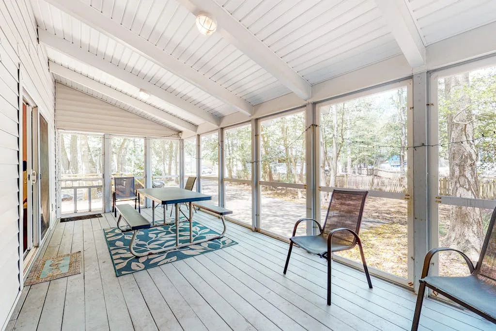 A bright enclosed porch with large windows, seating, and a table.