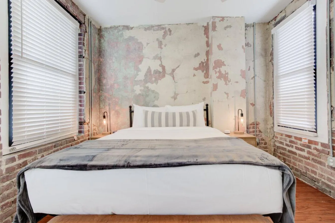 Un dormitorio con una cama centrada entre dos ventanas.