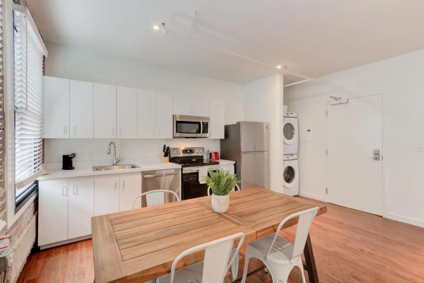 Una cocina abierta con zona de comedor, mesa de madera y armarios blancos.