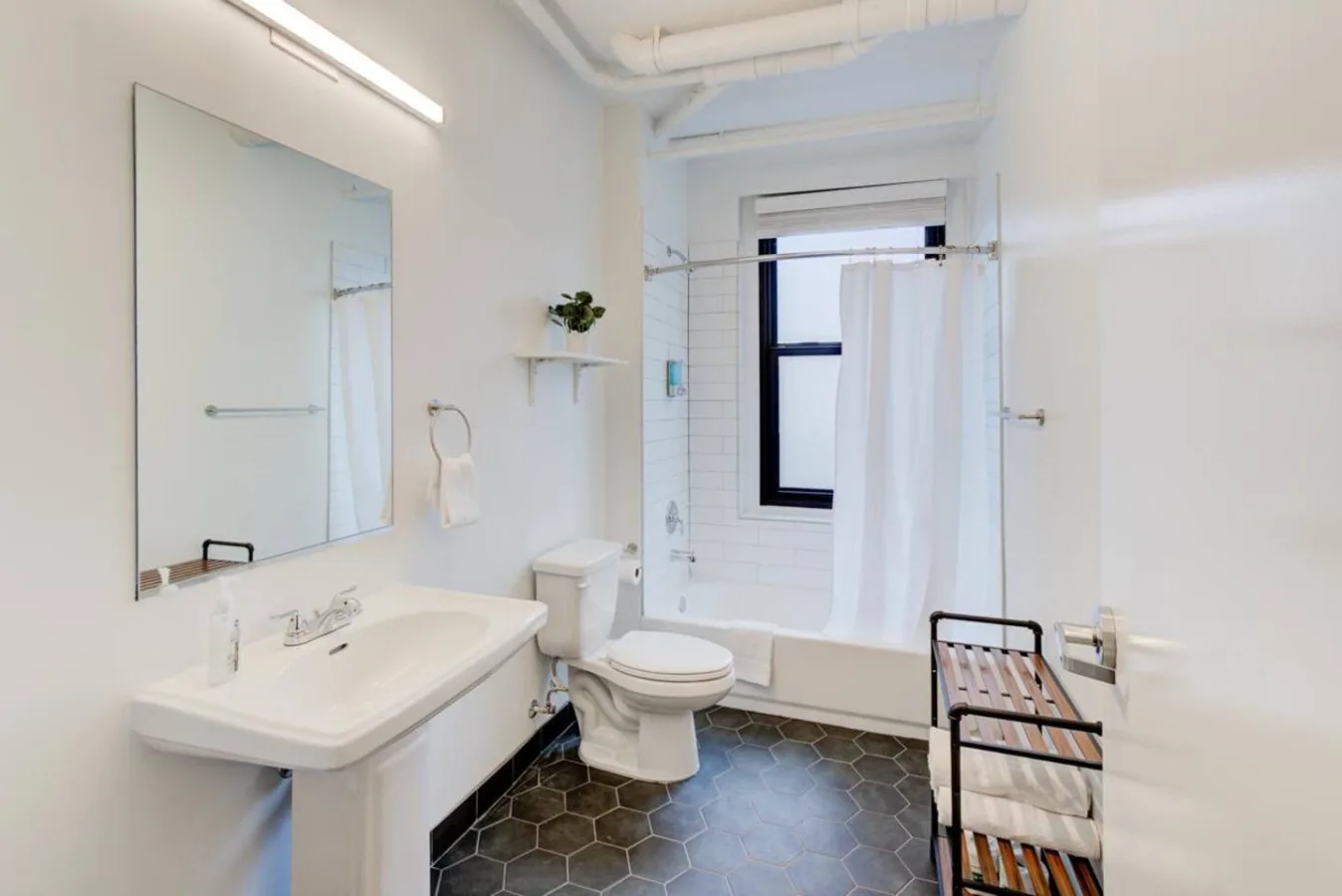 Un baño luminoso con lavabo, inodoro y bañera junto a una ventana con cortina.