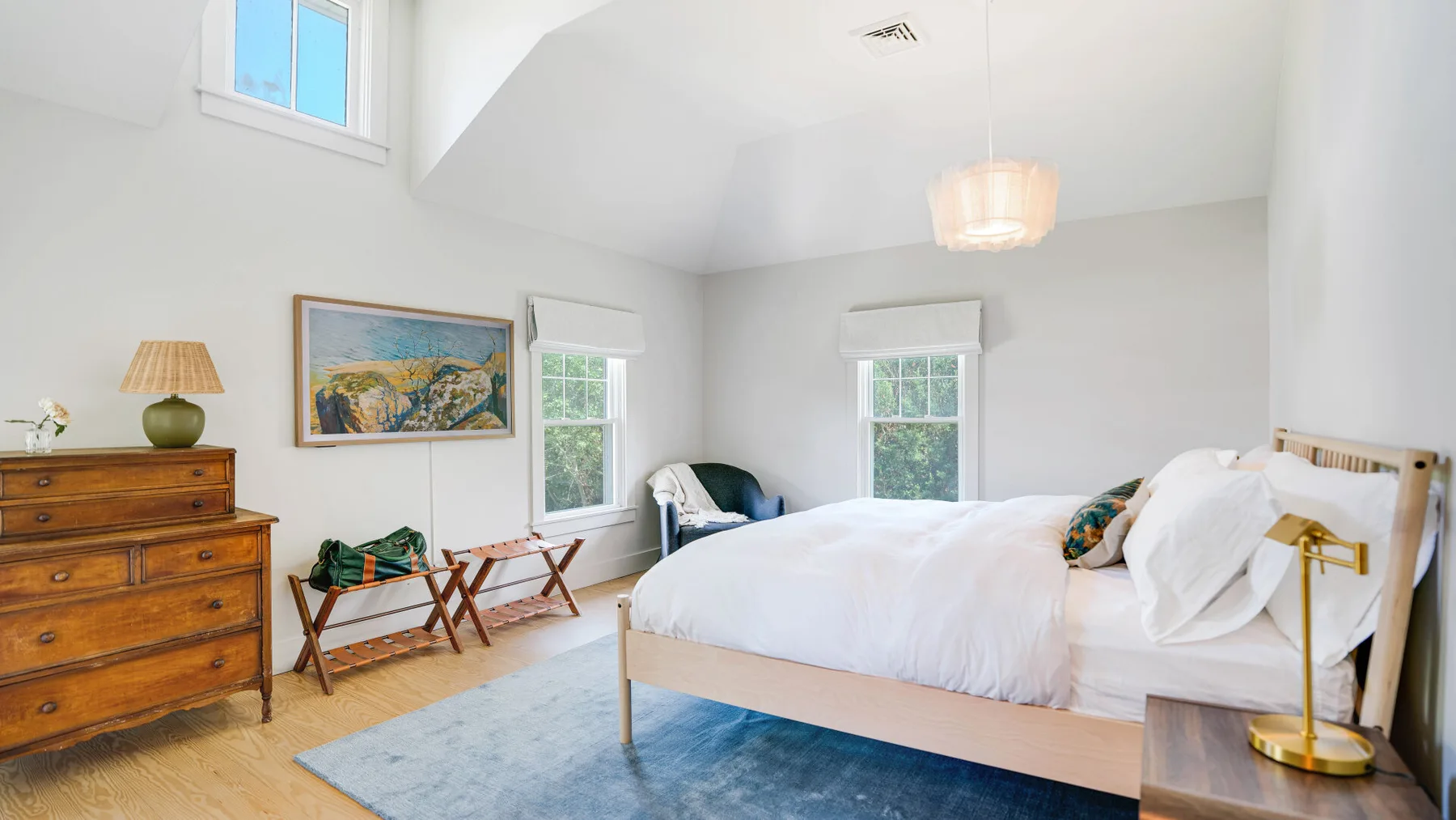A bright bedroom with a large bed, framed artwork, and a window.