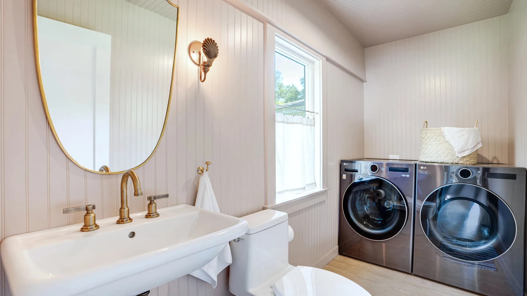 A bright laundry room with a washer and dryer beside a sink and toilet.