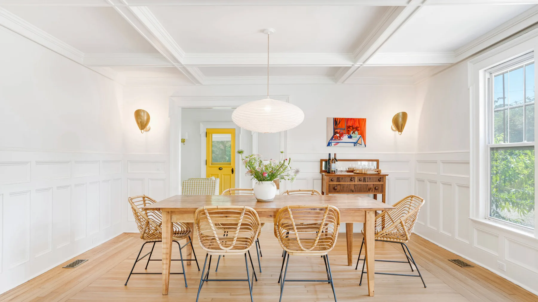 A bright dining room with a wooden table and chairs beneath a pendant light.