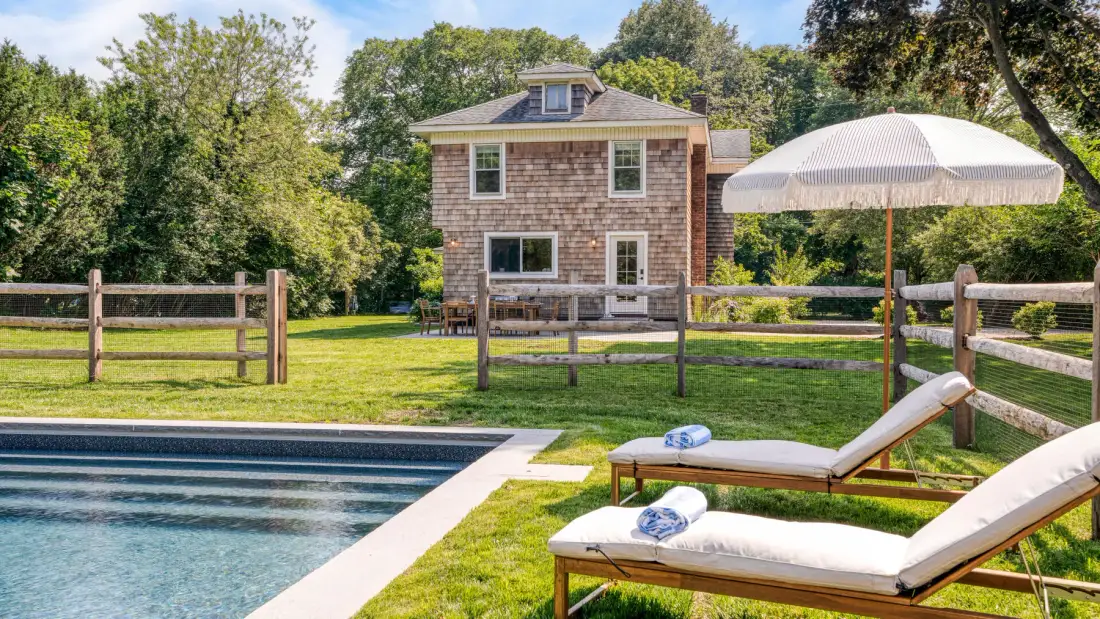 A backyard pool beside a lawn, lounge seating, and a shingled house.