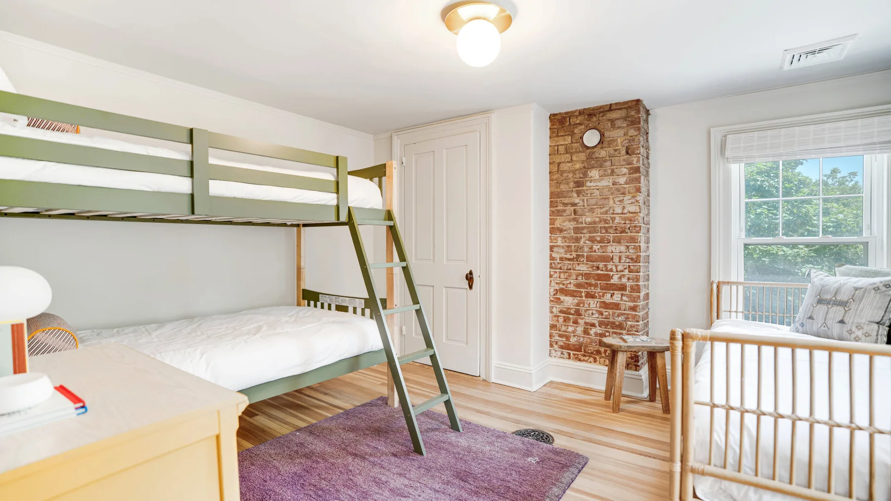 A bedroom with bunk beds, a crib, and a brick fireplace.