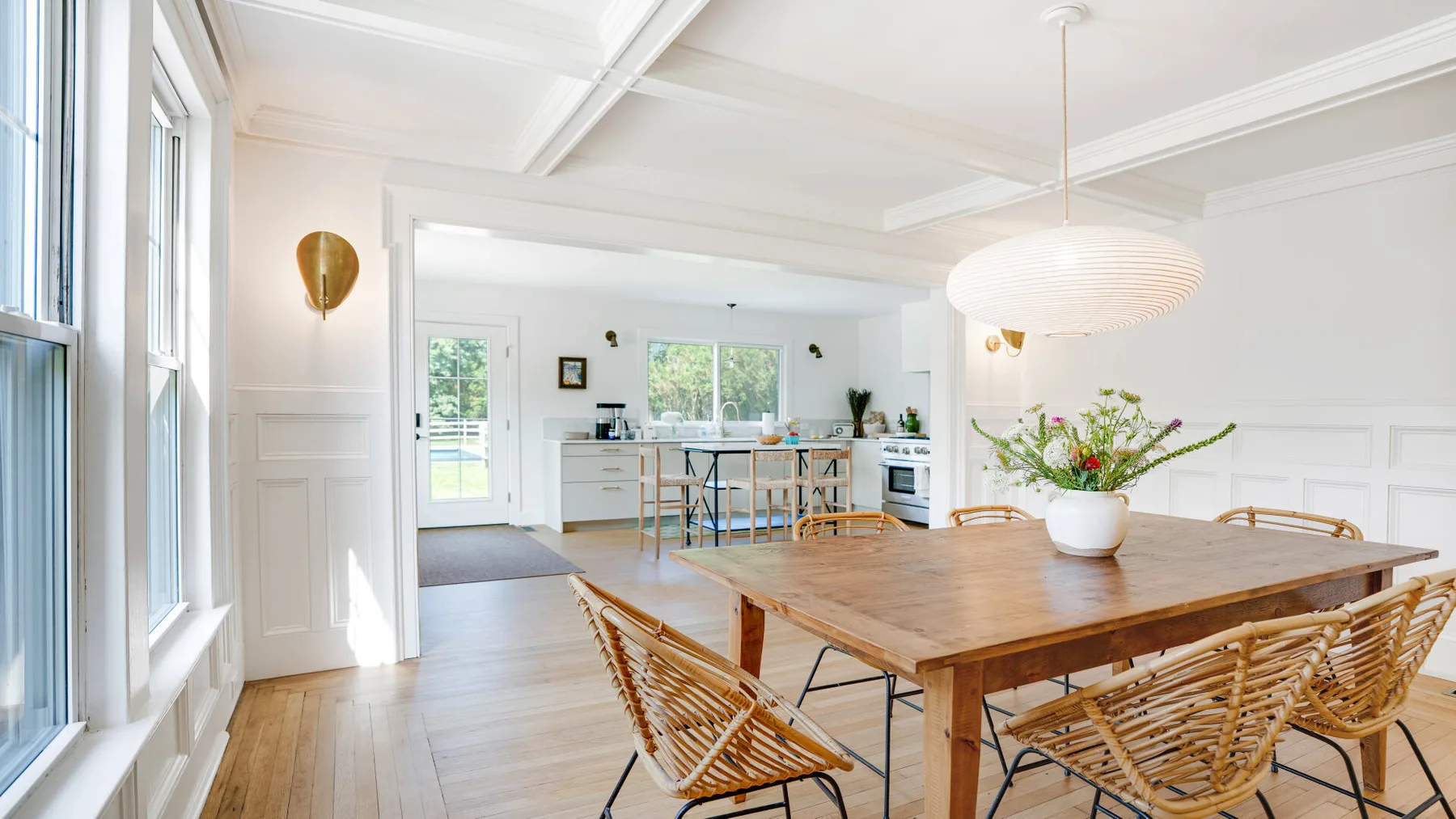 A bright dining area with a wooden table and an open kitchen beyond.