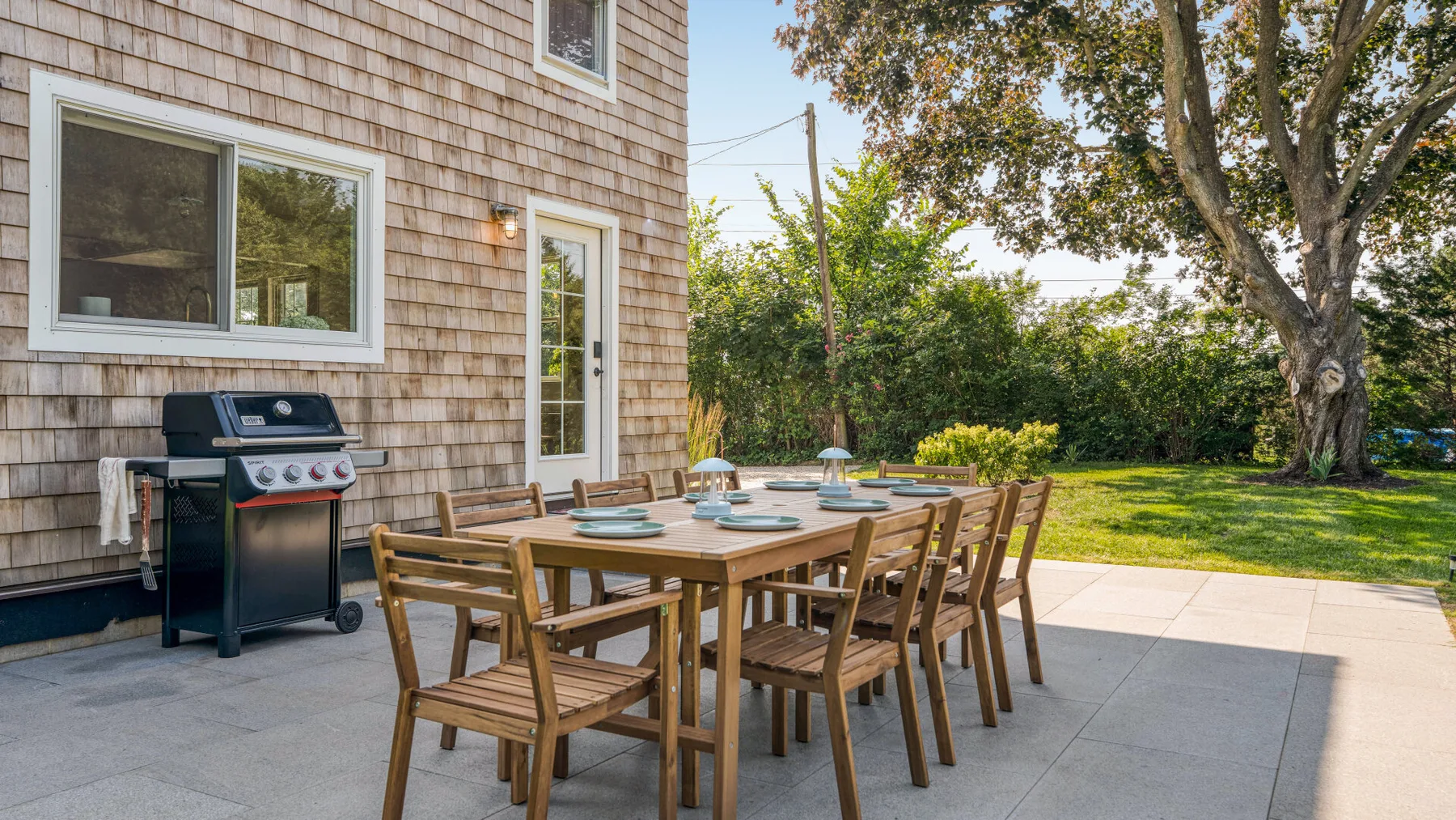 Una zona de comedor al aire libre con una mesa de madera y sillas junto a una casa.