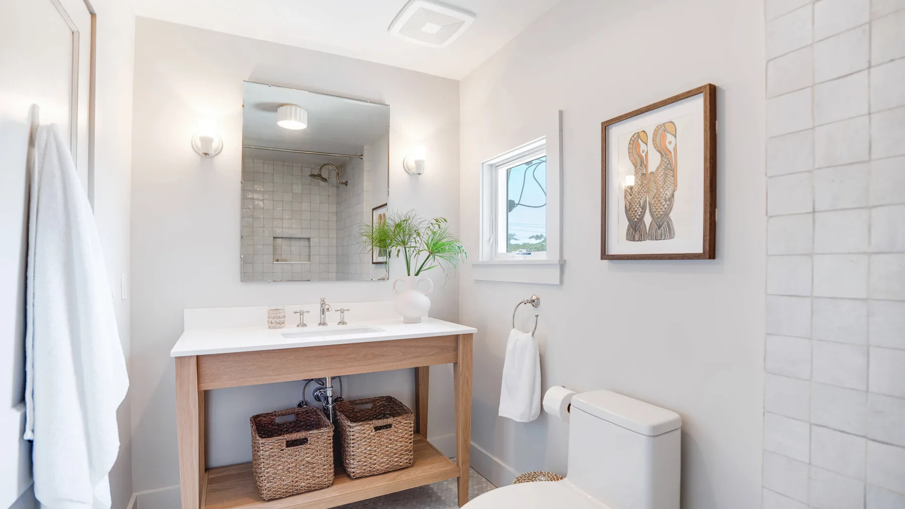 A bright bathroom with a vanity, framed artwork, and a window.
