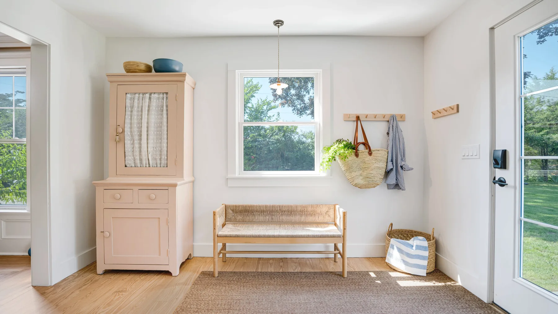 A bright entryway has a wooden bench beneath a window and hooks on the wall.