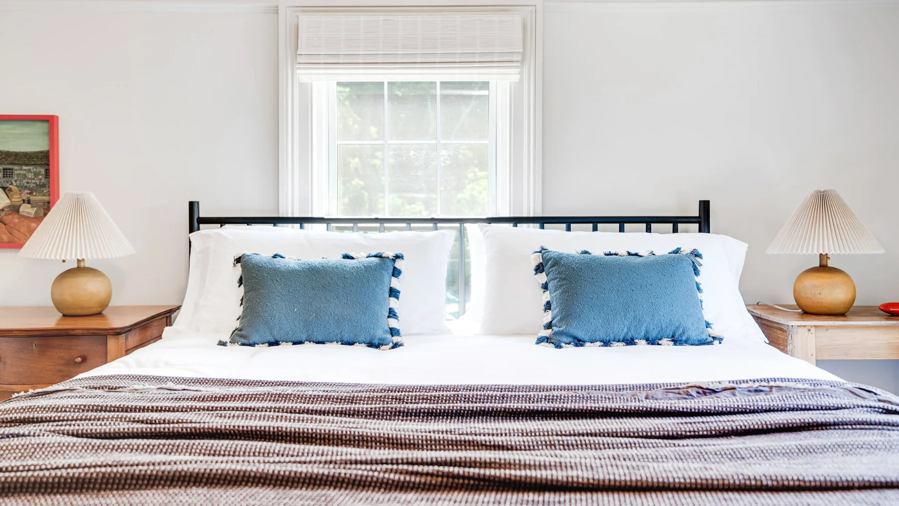 A bedroom with a neatly made bed, blue accent pillows, and a window behind it.