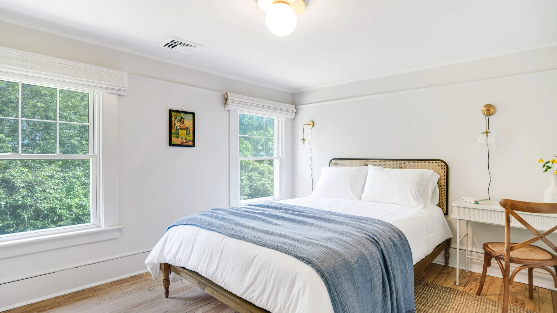 A bright bedroom with a neatly made bed and large windows.