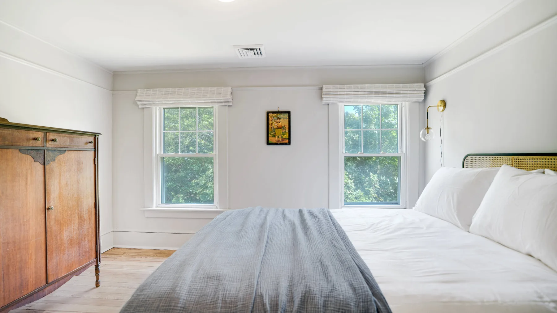 A bright bedroom with a neatly made bed and two windows.