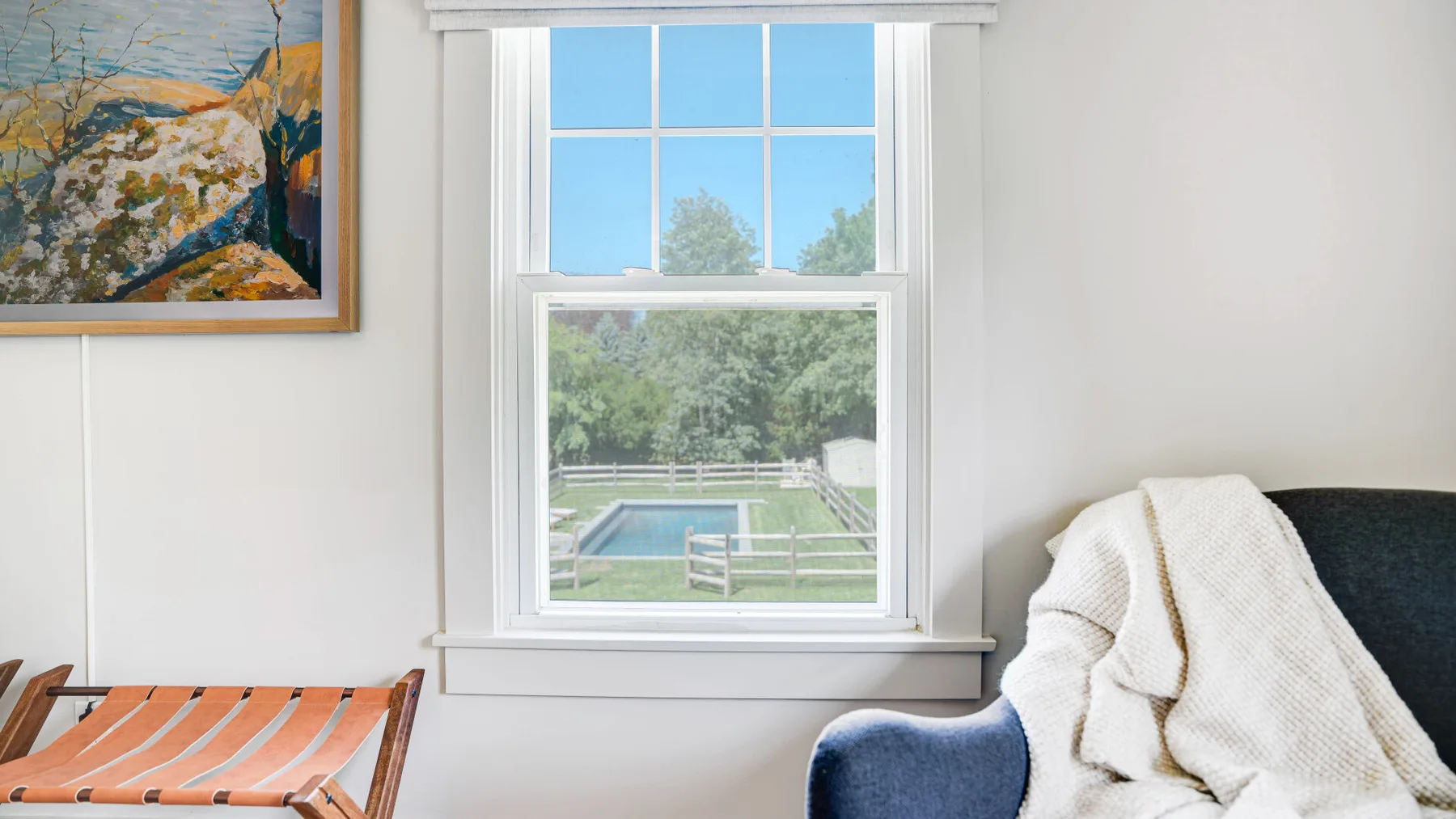 A seating area beside a window overlooking a garden and pool.