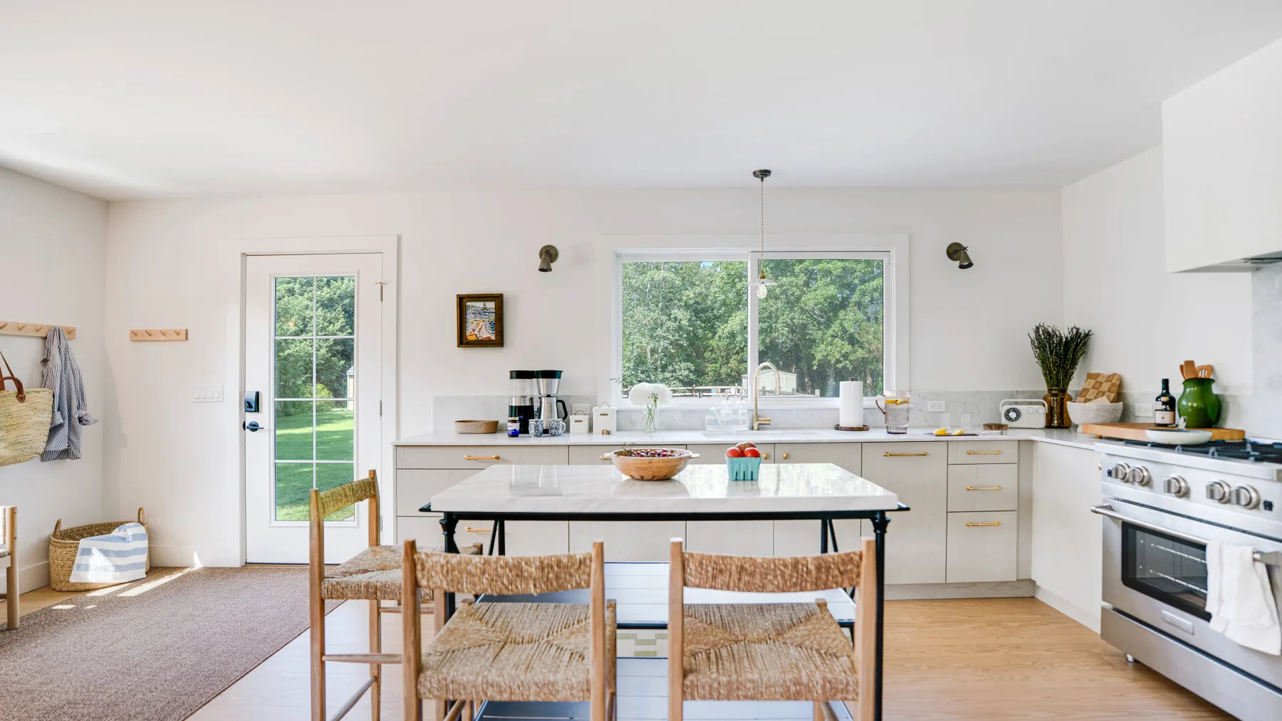 A bright kitchen with a dining table, broad windows, and white cabinetry.
