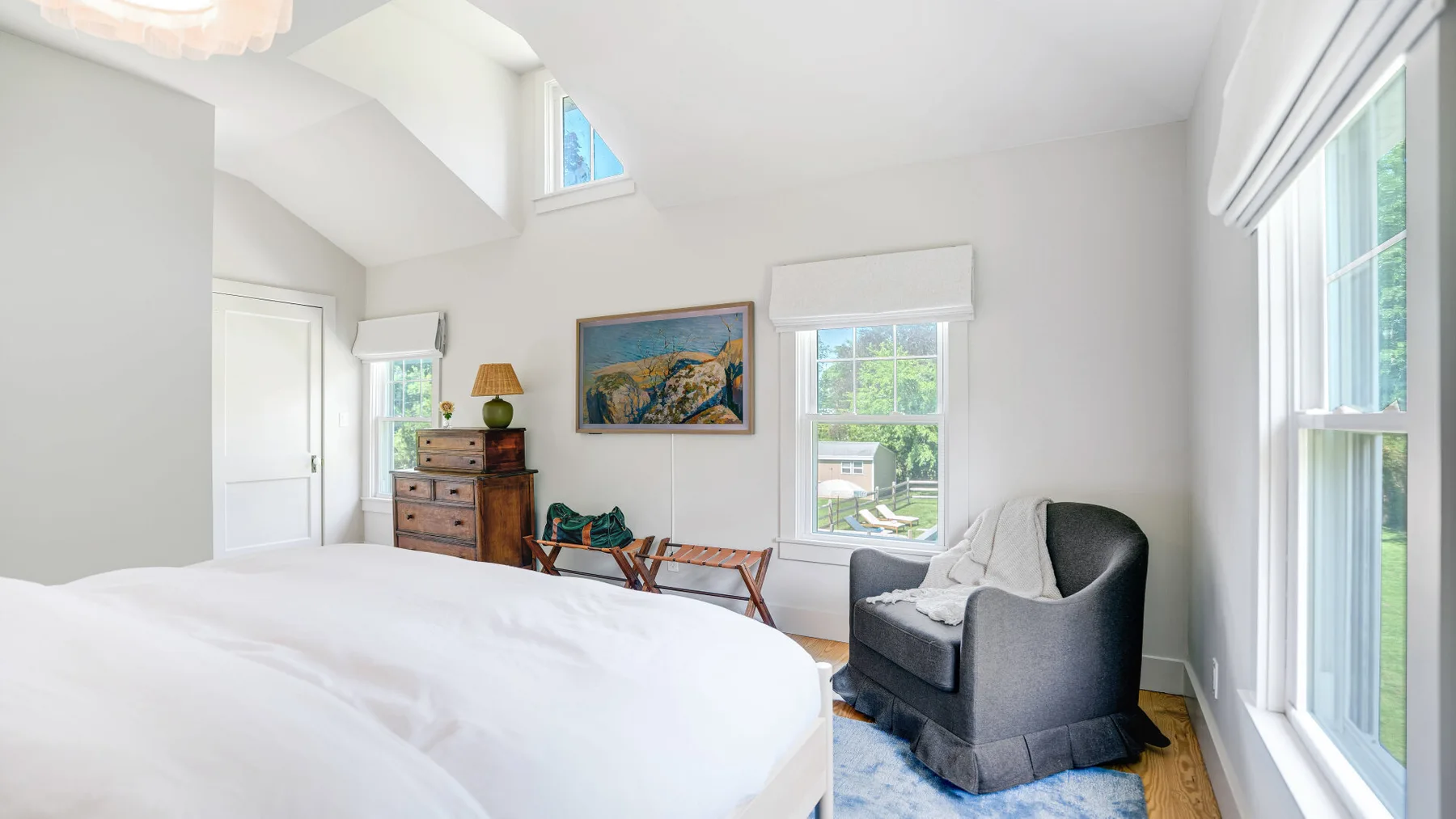 A bright bedroom with a bed, an armchair, and tall windows.