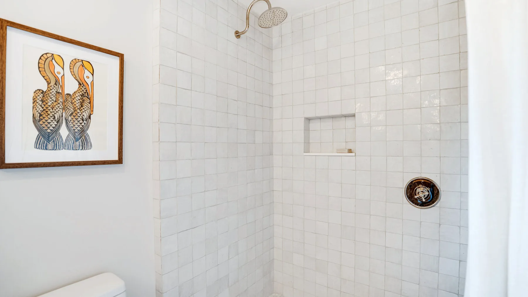 A tiled shower with a recessed shelf and framed bird artwork on the wall.