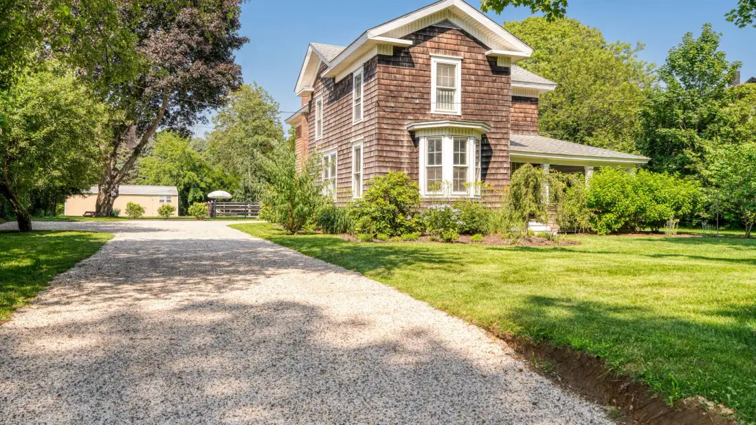 A brick house stands beside a curved gravel driveway and green lawn.