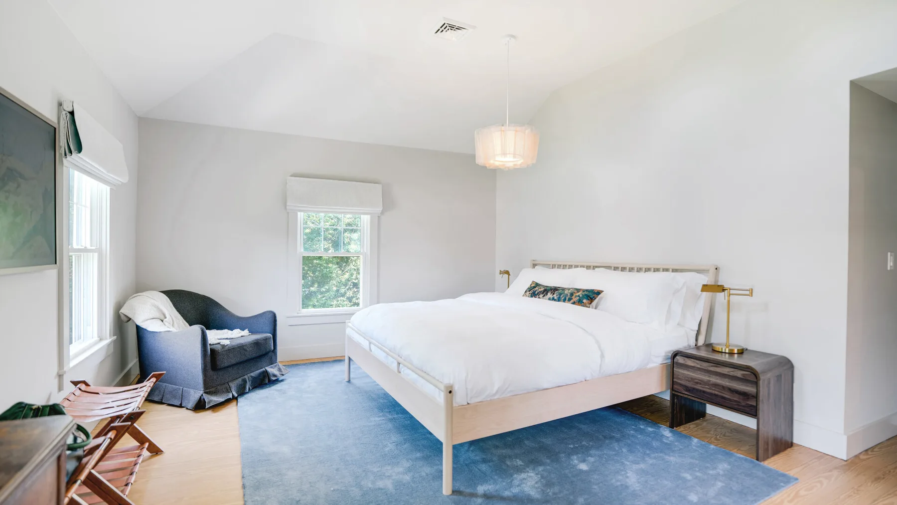 A bright bedroom with a large bed, blue rug, and windows.