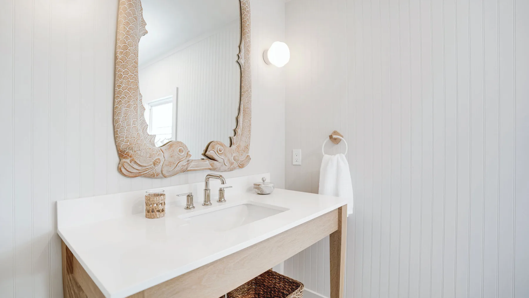 A bright bathroom vanity with a large decorative mirror and white paneled walls.