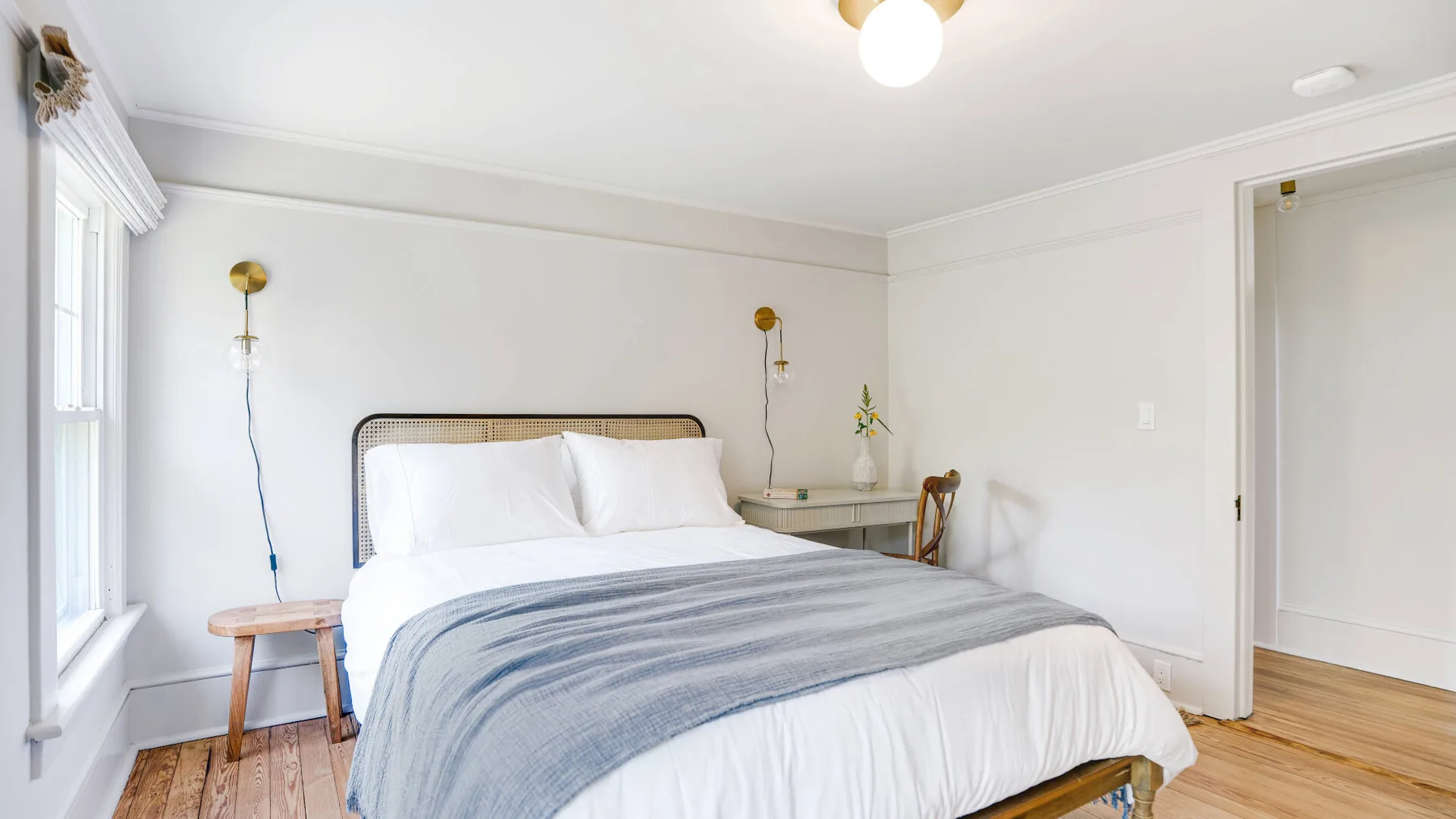 A bright bedroom with a neatly made bed and windows along one wall.