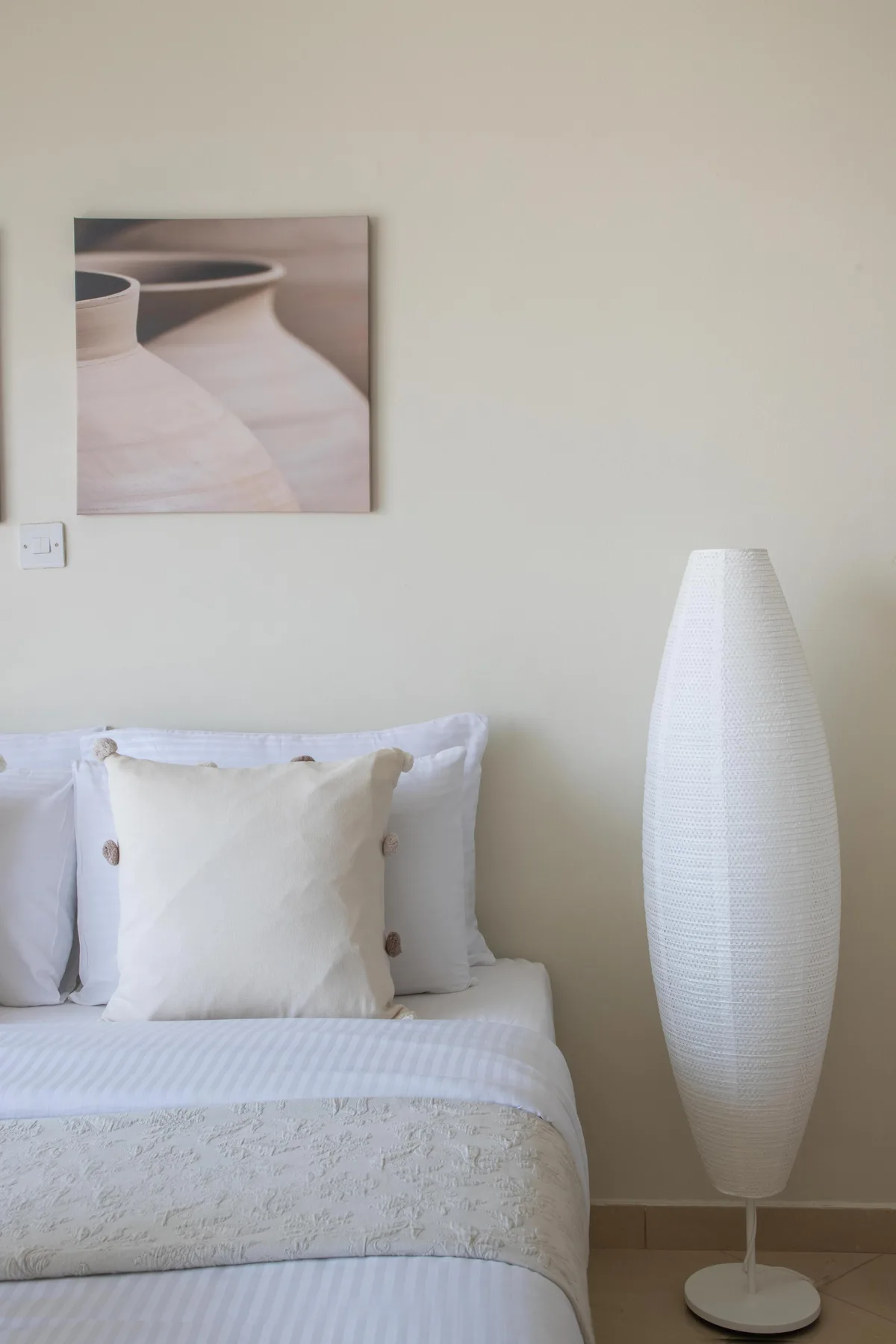 Un dormitorio con una cama bien tendida y una lámpara de pie alta al lado.