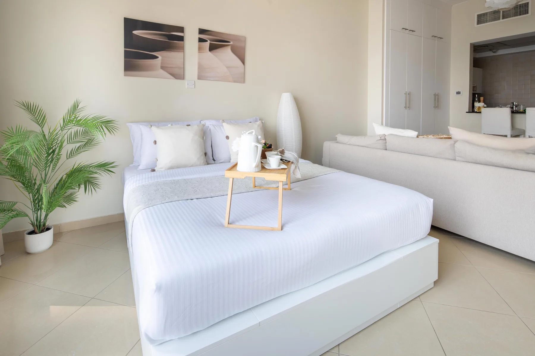 Un dormitorio luminoso con una cama tendida y una planta en maceta.