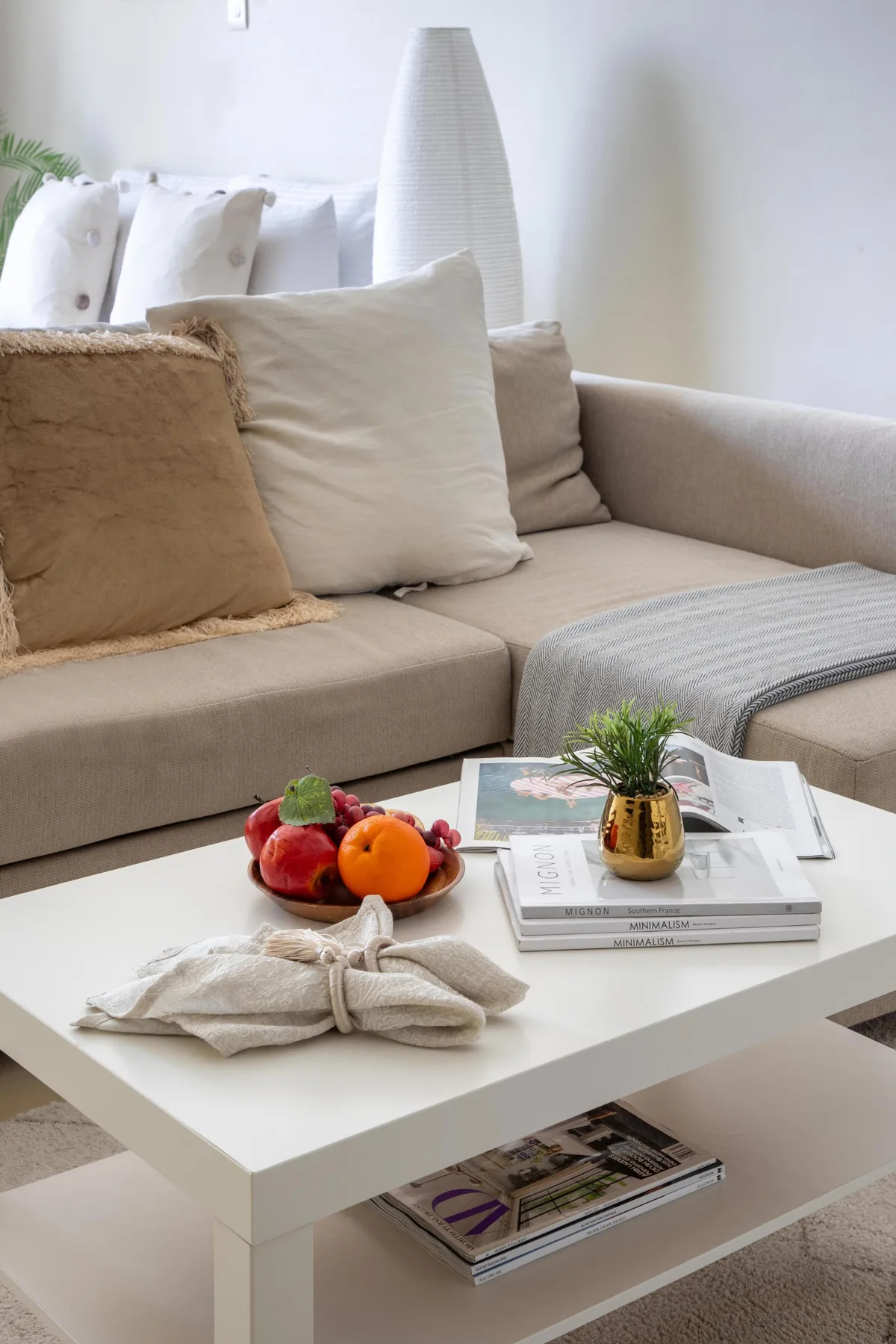 Una sala luminosa con un sofá beige y una mesa de centro con fruta y libros.