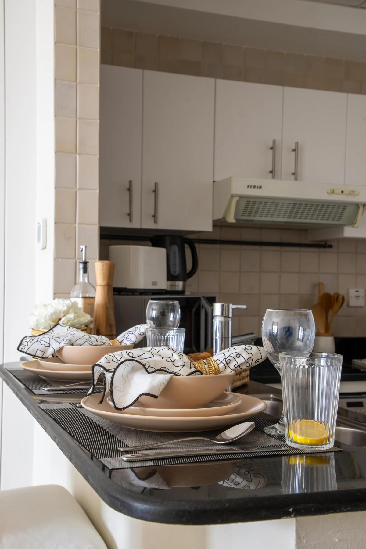Una encimera de cocina está preparada con platos y vasos bajo armarios blancos.