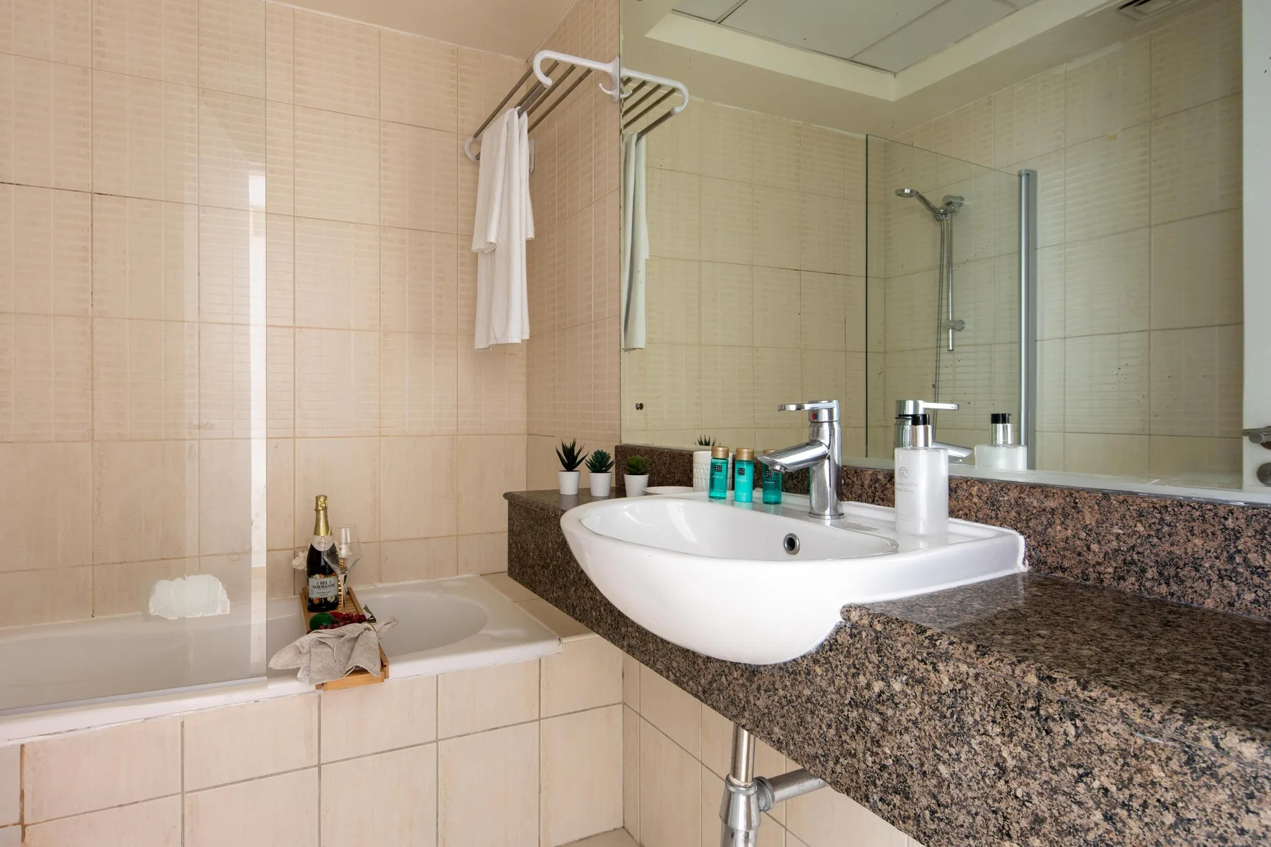 Un baño alicatado con bañera y lavabo sobre una encimera con acabado de piedra.