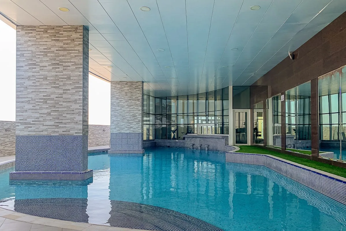 Una piscina cubierta bajo un techo, con paredes de vidrio a un lado.