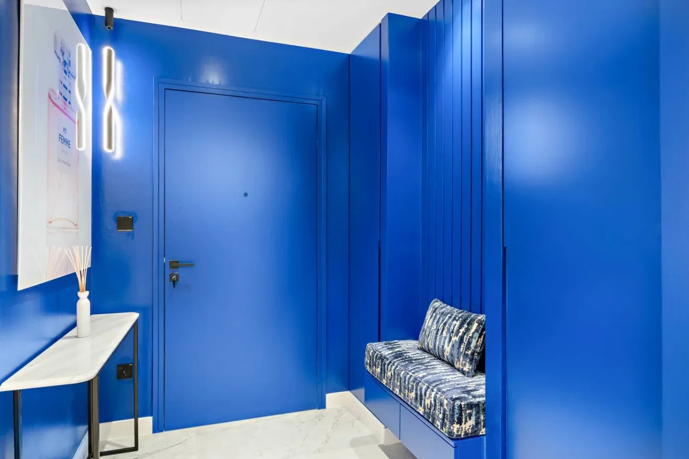 Una entrada azul brillante con una puerta, un banco estrecho y una pequeña mesa consola.