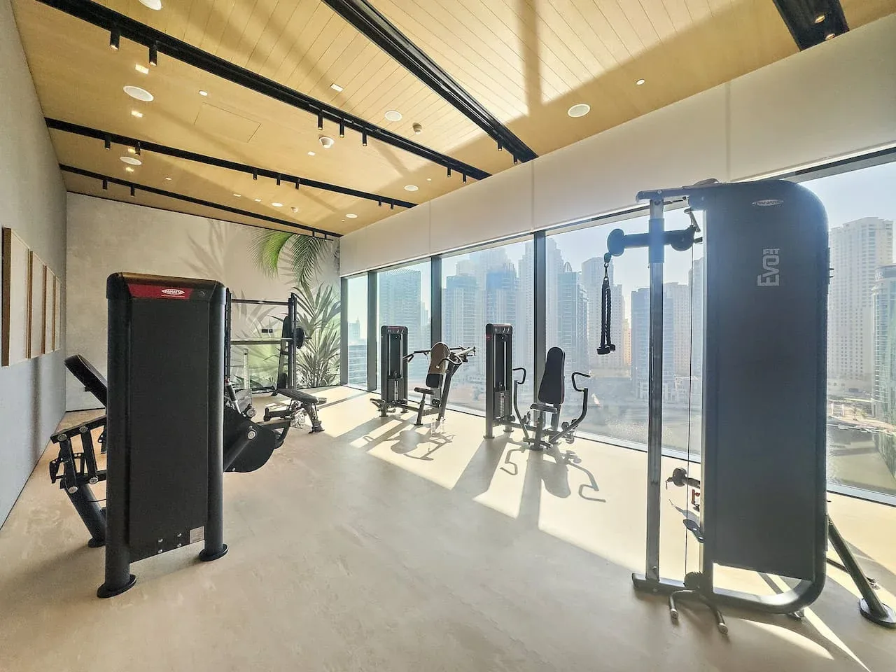 Un gimnasio luminoso con máquinas de ejercicio junto a grandes ventanales.