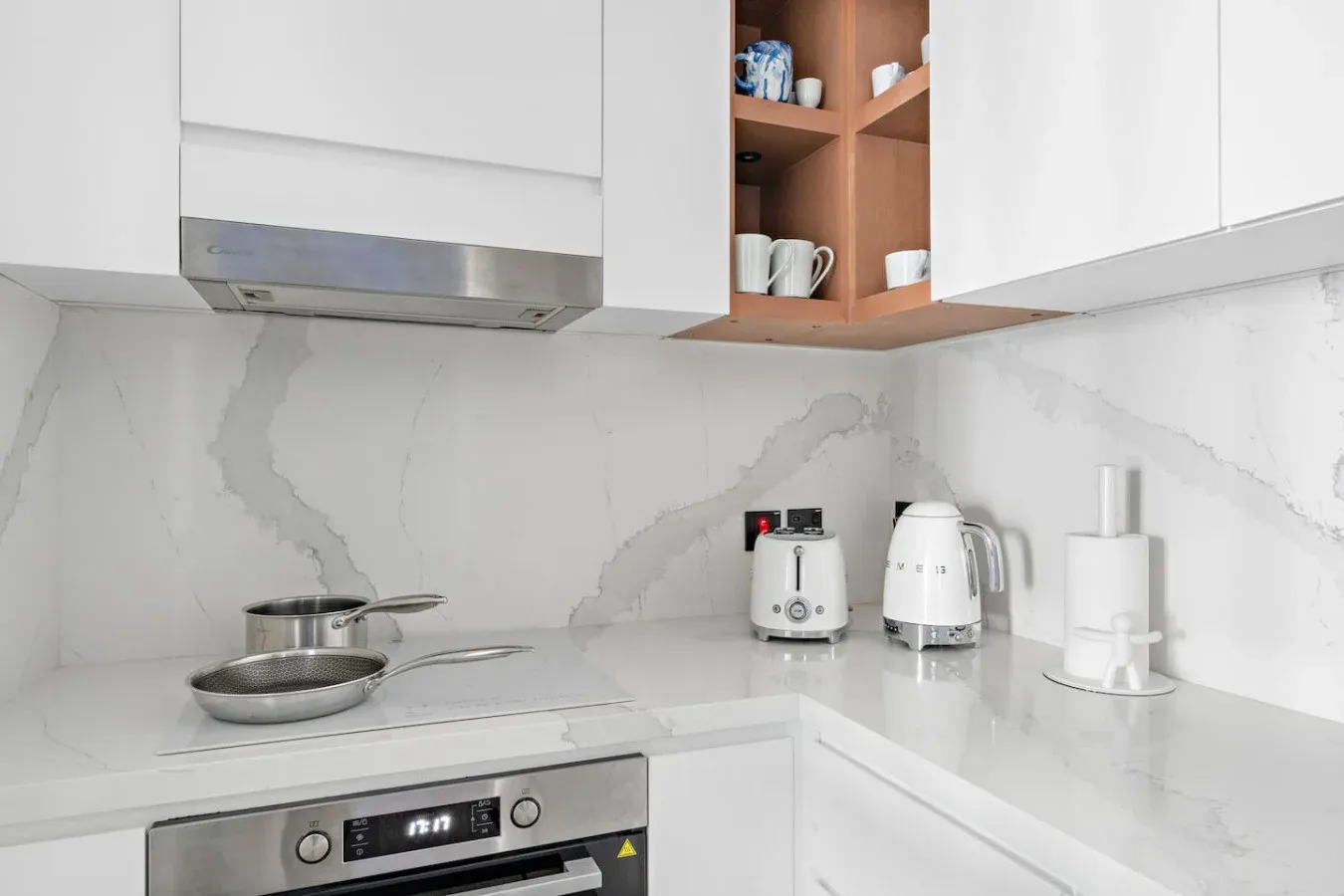 Una cocina luminosa con gabinetes blancos, una estufa y pequeños electrodomésticos.
