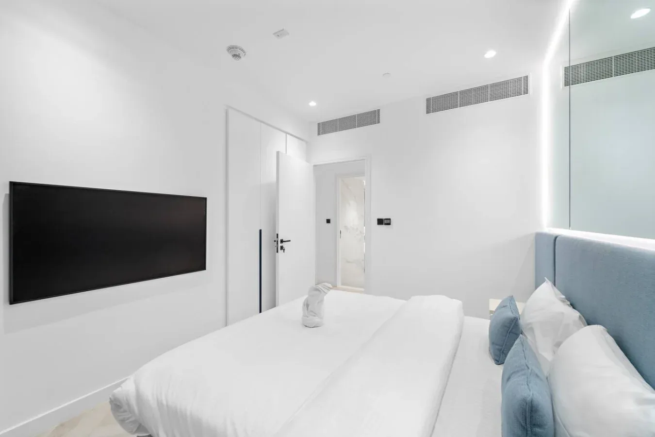Un dormitorio luminoso con ropa de cama blanca y un televisor en la pared.